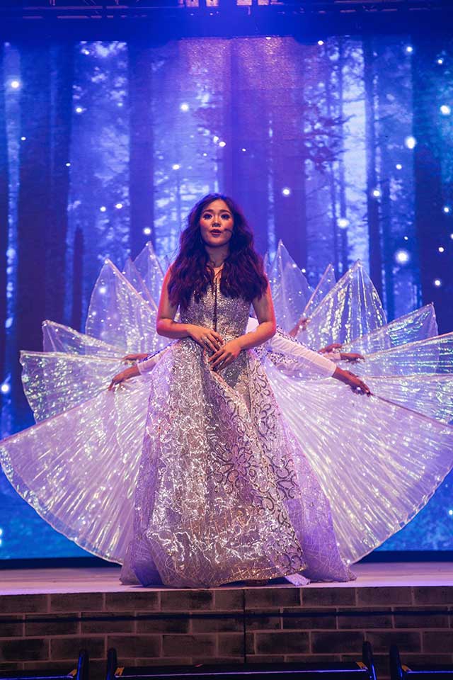 Alyanna Gopez wearing a sparkling gown on stage at her debut, orchestrated by the Spouses Gopez, with luminous wing-like props behind her